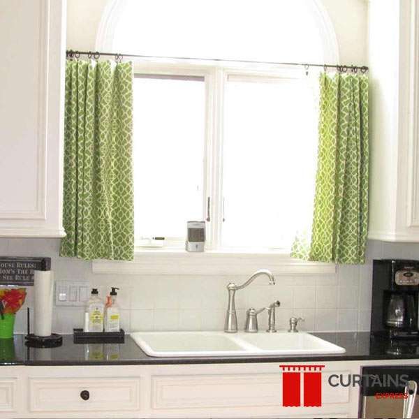 Short green trellis-print cafe curtains on a black rod across an arched window above a kitchen sink