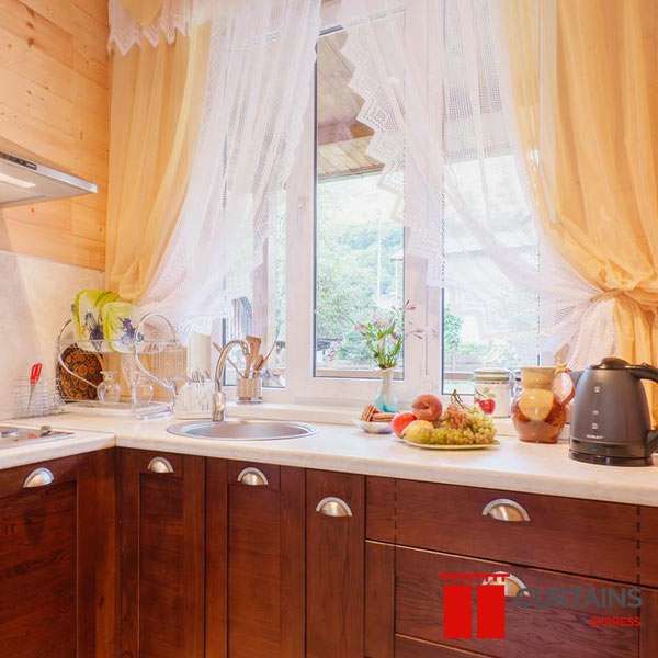 White lace-edged sheers tied back on both sides of a kitchen window above the sink in a timber-clad cottage kitchen