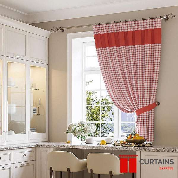 Red and white gingham curtain with a solid red top band, tied back at a cream kitchen window on a metal pole