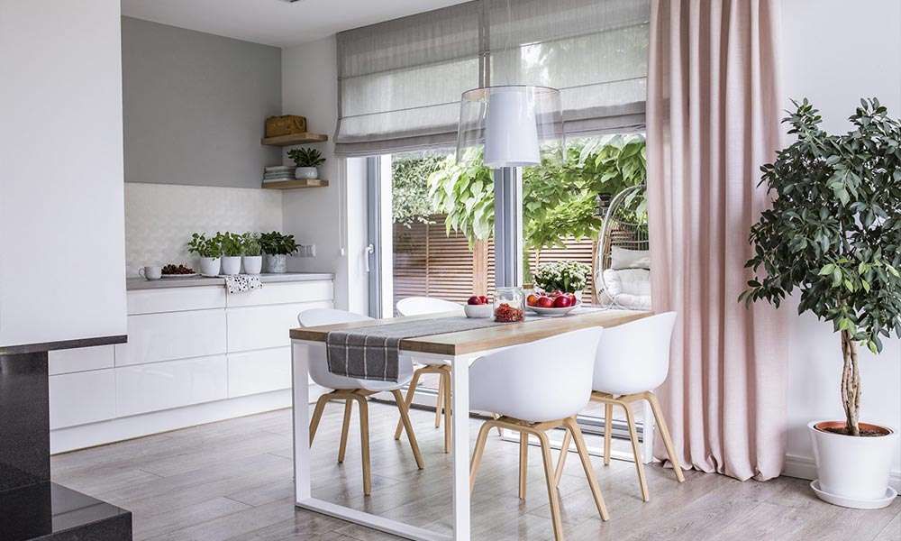 Blush pink floor-length curtain beside patio doors in a white kitchen-diner, a grey roman blind half lowered above