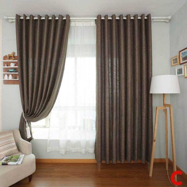 Brown eyelet curtains on a white pole, left panel tied back over a white sheer, in a room with a tripod floor lamp