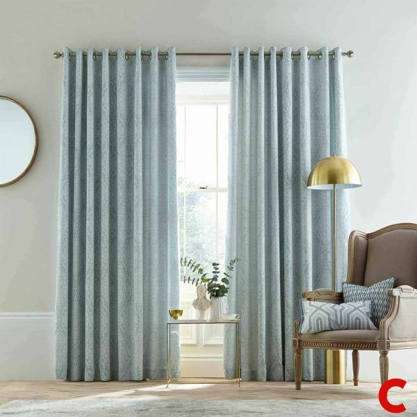 Duck-egg blue eyelet curtains with a leaf jacquard weave on a steel pole, framing a sash window beside a gold lamp