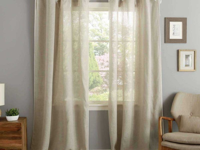 Semi-transparent flax linen eyelet curtains nearly closed over a window, greenery visible through the loose weave