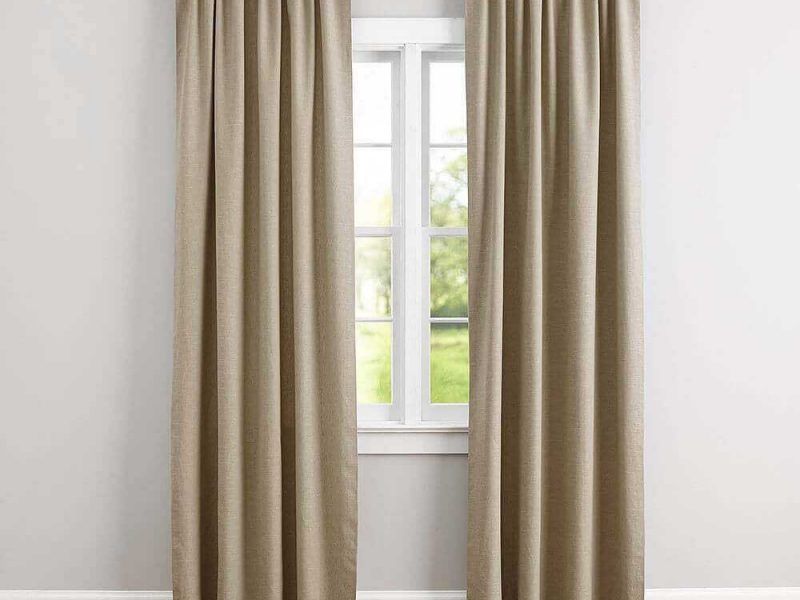 Plain taupe linen curtains hanging floor to ceiling either side of a small white casement window on a grey wall