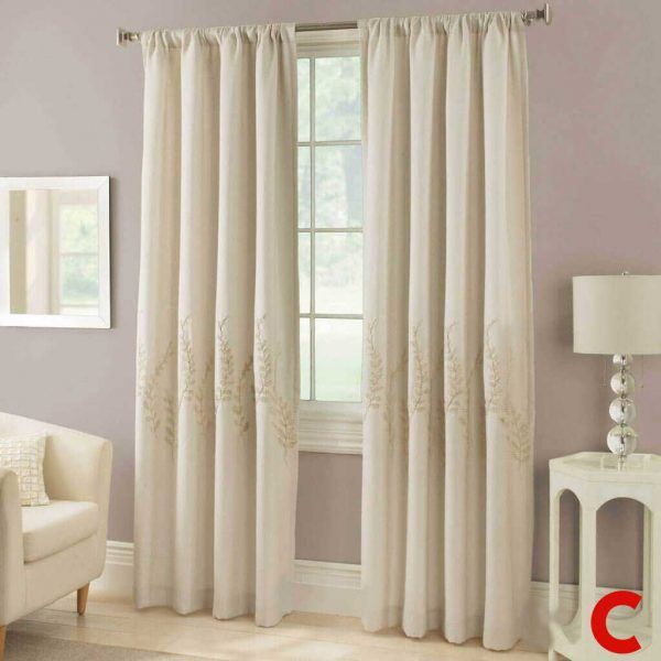 Ivory pencil-pleat curtains embroidered with a wheat motif near the hem, at a window in a lilac-walled sitting room