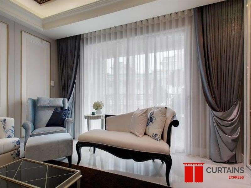 Silver-grey satin curtains gathered into a swag over floor-length white sheers at a balcony door, behind a chaise