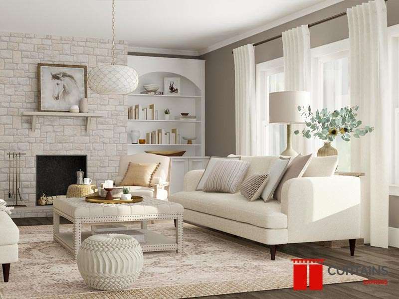 Ivory curtains hung high on a dark rod either side of the windows in a cream living room with a stone fireplace