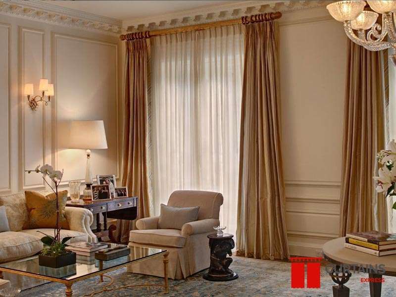 Champagne striped silk curtains on a wooden ring pole over a white sheer, in a panelled room with a chandelier