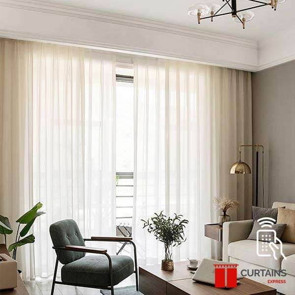 Cream sheer curtains drawn full width across a balcony door, with a taupe side curtain and a green armchair