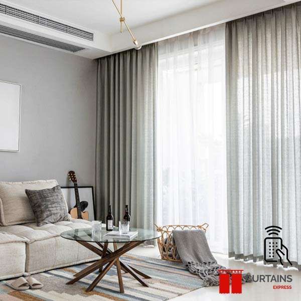Sage-grey curtains on a ceiling track flanking a white sheer at a tall balcony window, with a rattan chair nearby