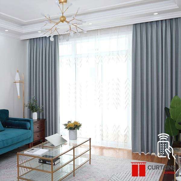 Grey curtains framing a white patterned sheer at a balcony door, with a teal sofa and gold glass coffee table