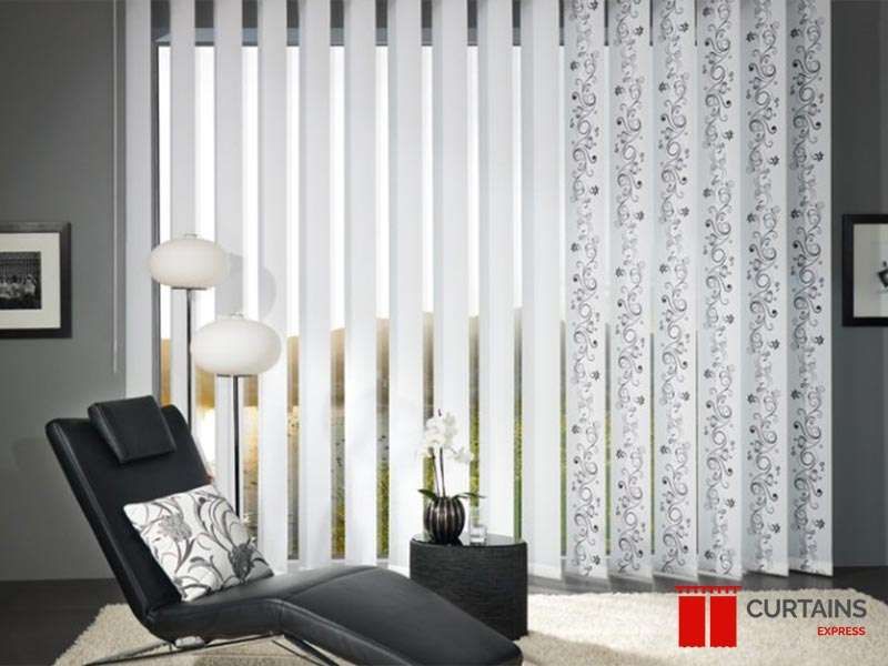 Vertical blinds combining plain white and grey floral-patterned slats behind a black leather chaise longue
