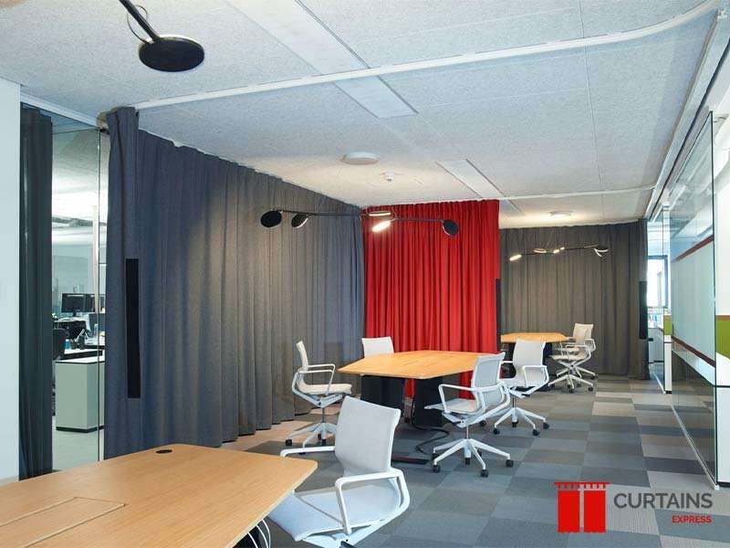 Grey curtains on ceiling tracks partitioning meeting tables in an open-plan office, with one red curtain