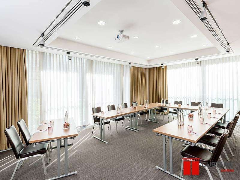 White sheers with gold side curtains along a conference-room window wall behind U-shaped tables and black chairs