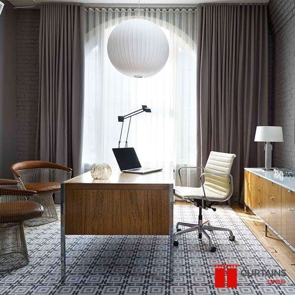 Mauve-grey curtains and a white sheer over an arched window in a brick-walled home office with a globe pendant
