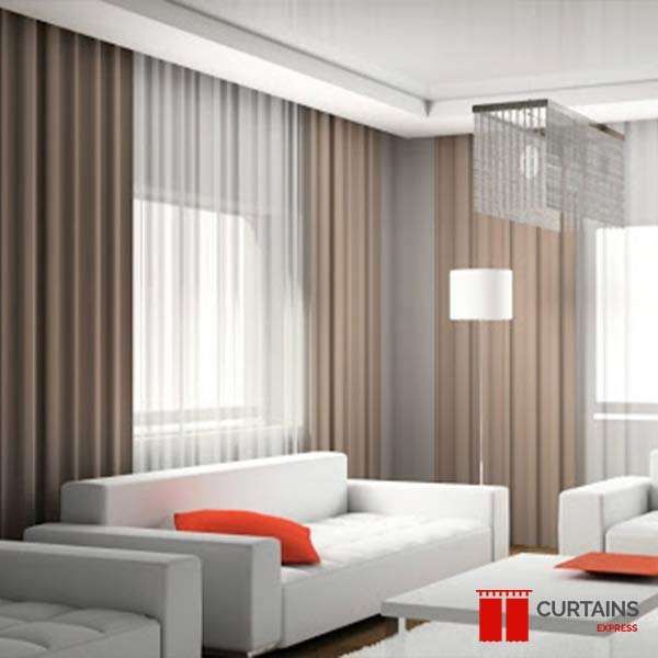 White leather sofas with orange cushions in front of taupe curtains and sheers covering two window walls