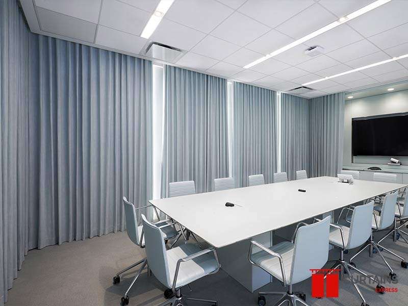 Pale blue-grey curtains closed along two boardroom walls behind a white table and light blue chairs