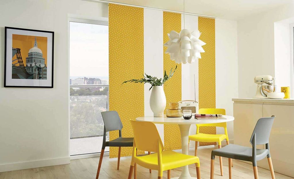 Yellow polka-dot sliding panel blinds drawn across a balcony door beside a white dining table