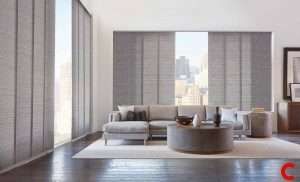 Grey woven panel blinds across a high-rise window wall, one panel slid aside to show the city beyond