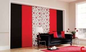 Black, red and rose-patterned sliding panel blinds across a wide window above a black velvet sofa