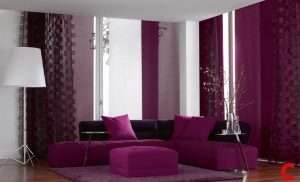 Plain and patterned magenta panel blinds across two window walls behind a purple sectional and ottoman