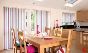 Pink and green striped vertical blinds across patio doors in a wooden kitchen-diner, repeated at the kitchen window