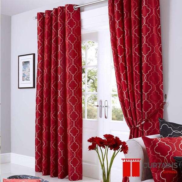 Deep red eyelet curtains printed with a white trellis motif, on a chrome pole across white French doors