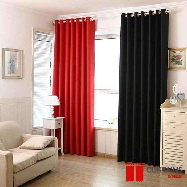 A red and a black eyelet panel sharing one pole at a corner window, white venetian blind behind