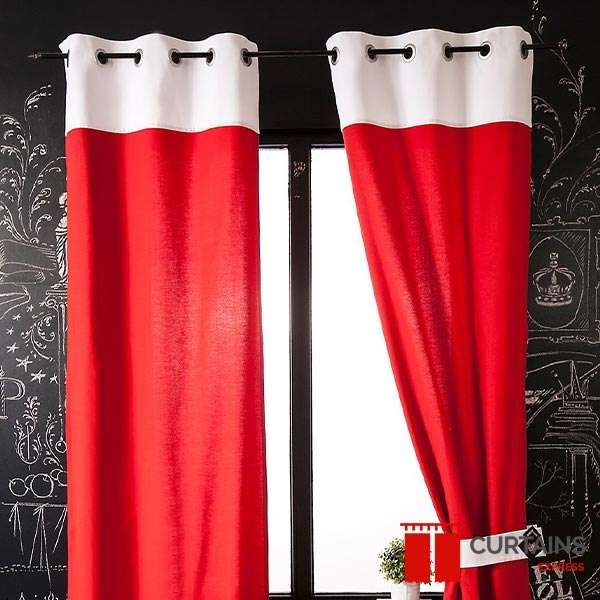 Red eyelet curtains with a cream contrast top band on a black rod against a chalkboard-painted wall