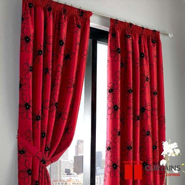 Red pencil-pleat curtains with a black flock floral print, one panel tied back over a city skyline view