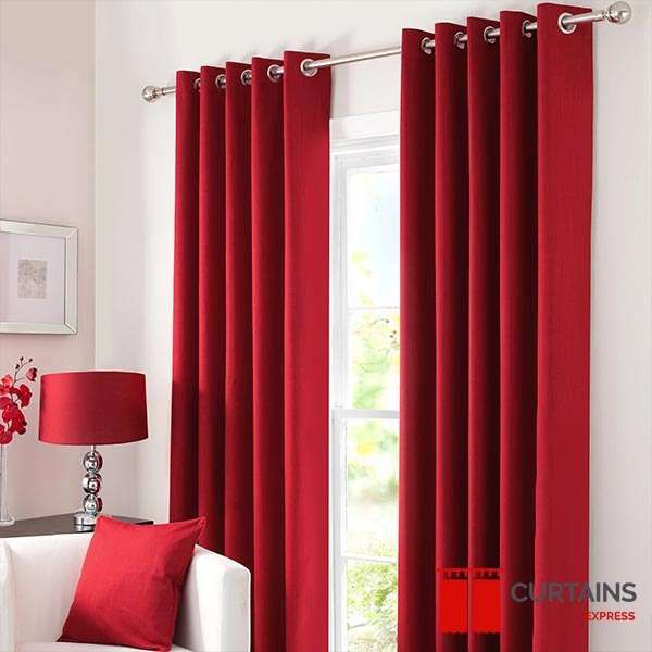 Plain deep red eyelet curtains on a chrome pole above a white sofa with a matching red cushion