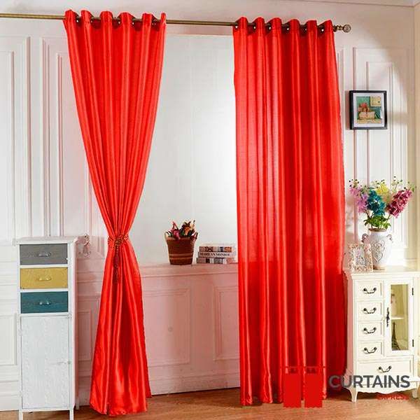 Bright red satin eyelet curtains on a bronze pole, the left panel gathered into a tie-back
