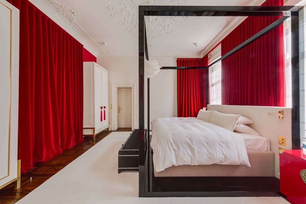 Full-height red velvet curtains covering two walls of a bedroom with a black four-poster bed and white bedding