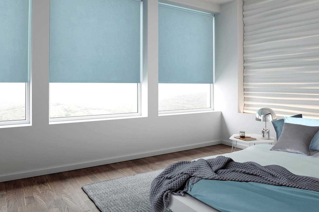 Pale blue roller blinds three-quarters lowered over three bedroom windows, a cream pleated shade alongside