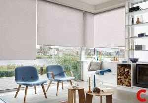 Blush textured roller blinds half lowered over balcony glass doors, above two blue moulded chairs