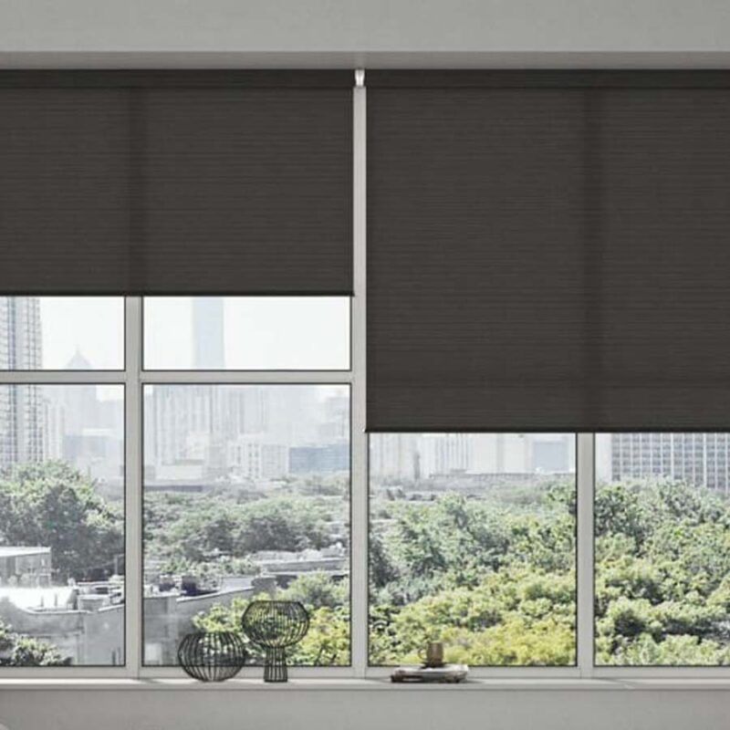 Charcoal roller blinds hanging at uneven heights across a corner window, wire vases on the sill