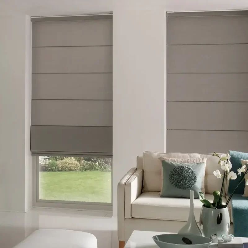 Warm grey roman blinds lowered almost to the sill on two windows, a lawn visible under the left one