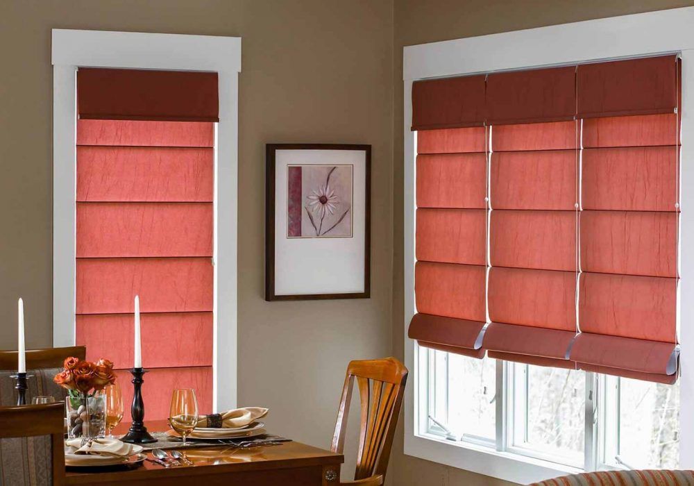 Coral roman blinds on a tall narrow window and a wide one in a taupe dining corner set with candles