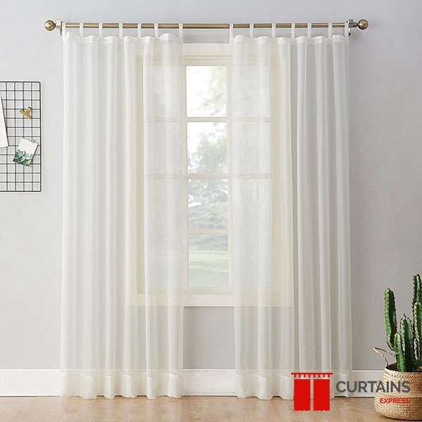 Ivory tab-top sheer curtains on a brass pole across a white sash window, a cactus in a basket alongside