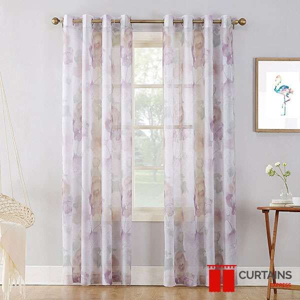 Sheer eyelet curtains printed with mauve watercolour flowers on a brass pole over a small window