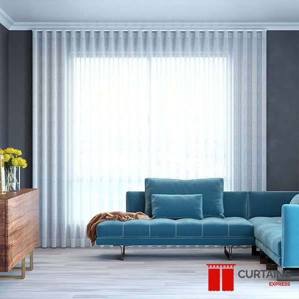 White sheer curtains gathered across a wide living room window behind a teal velvet corner sofa and walnut sideboard