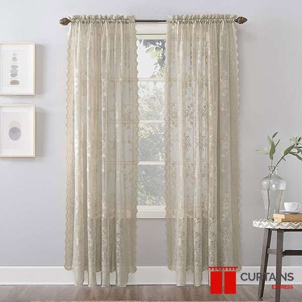 Cream lace sheer panels with scalloped edges on a bronze rod flanking a narrow sash window beside framed prints