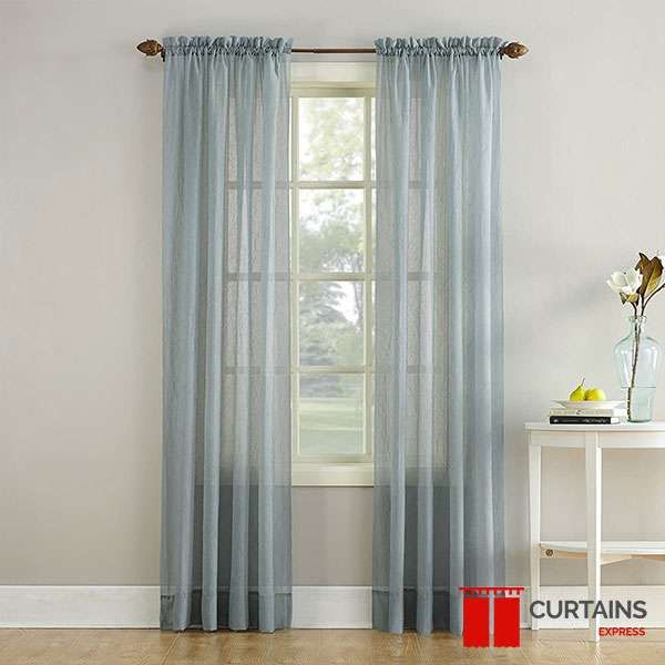 Dusty blue sheer panels on a bronze pole either side of a small sash window, with a white console table alongside