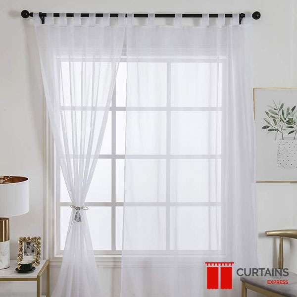 White tab-top sheer curtains on a black rod at a bedroom window, one panel held by a tasselled tieback