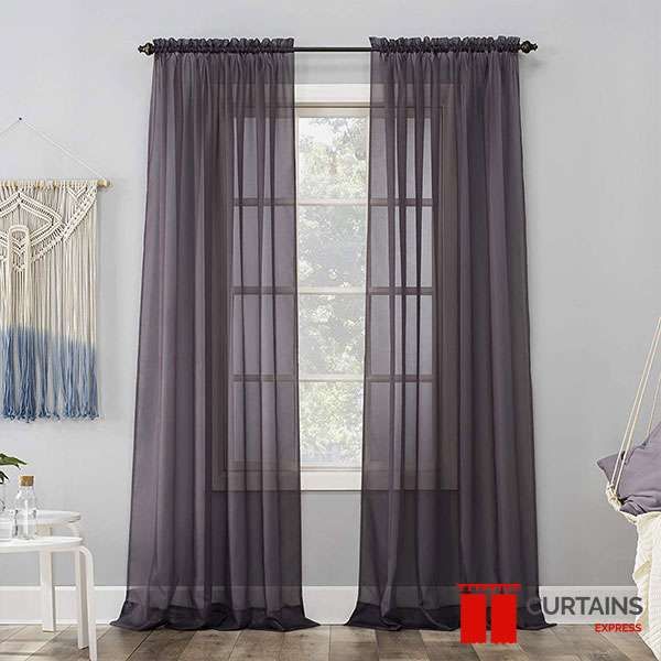Deep aubergine sheer panels on a black rod at a window, with a macrame wall hanging and hanging chair nearby