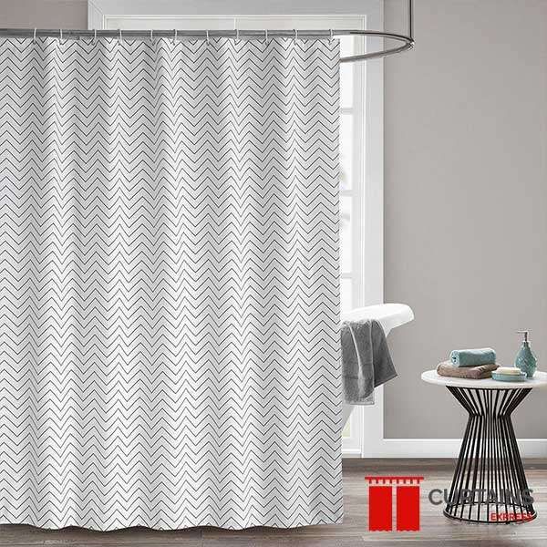White shower curtain in a fine grey zigzag print on a curved chrome rail against a grey wall