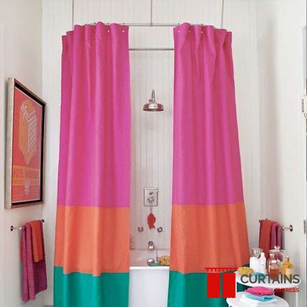 Pink, orange and green colour-blocked shower curtains parted either side of a bath with an exposed shower head