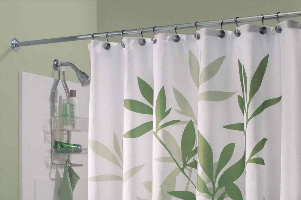 White shower curtain printed with green bamboo leaves on a chrome rod against a sage-green bathroom wall