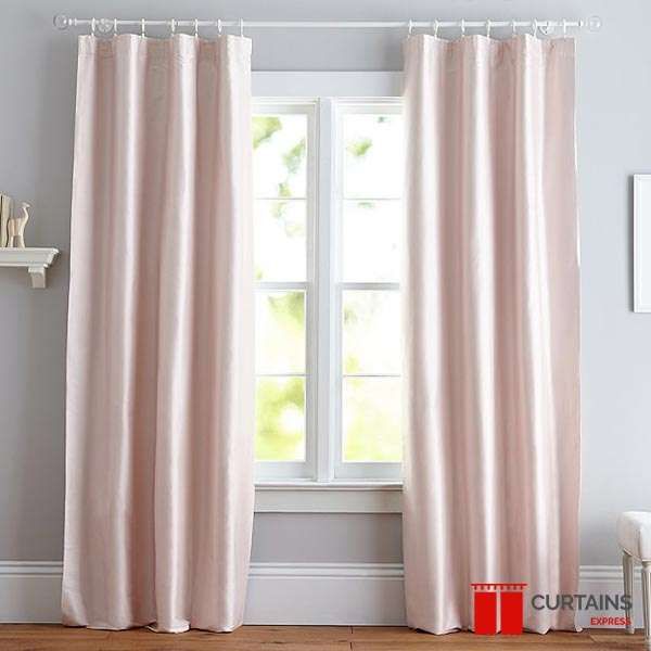 Blush pink tab-top curtains on a white pole either side of a small casement window above a wooden floor