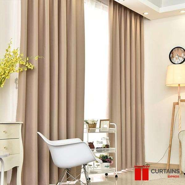 Taupe floor-to-ceiling curtains on a recessed ceiling track with a white sheer behind, beside a moulded chair